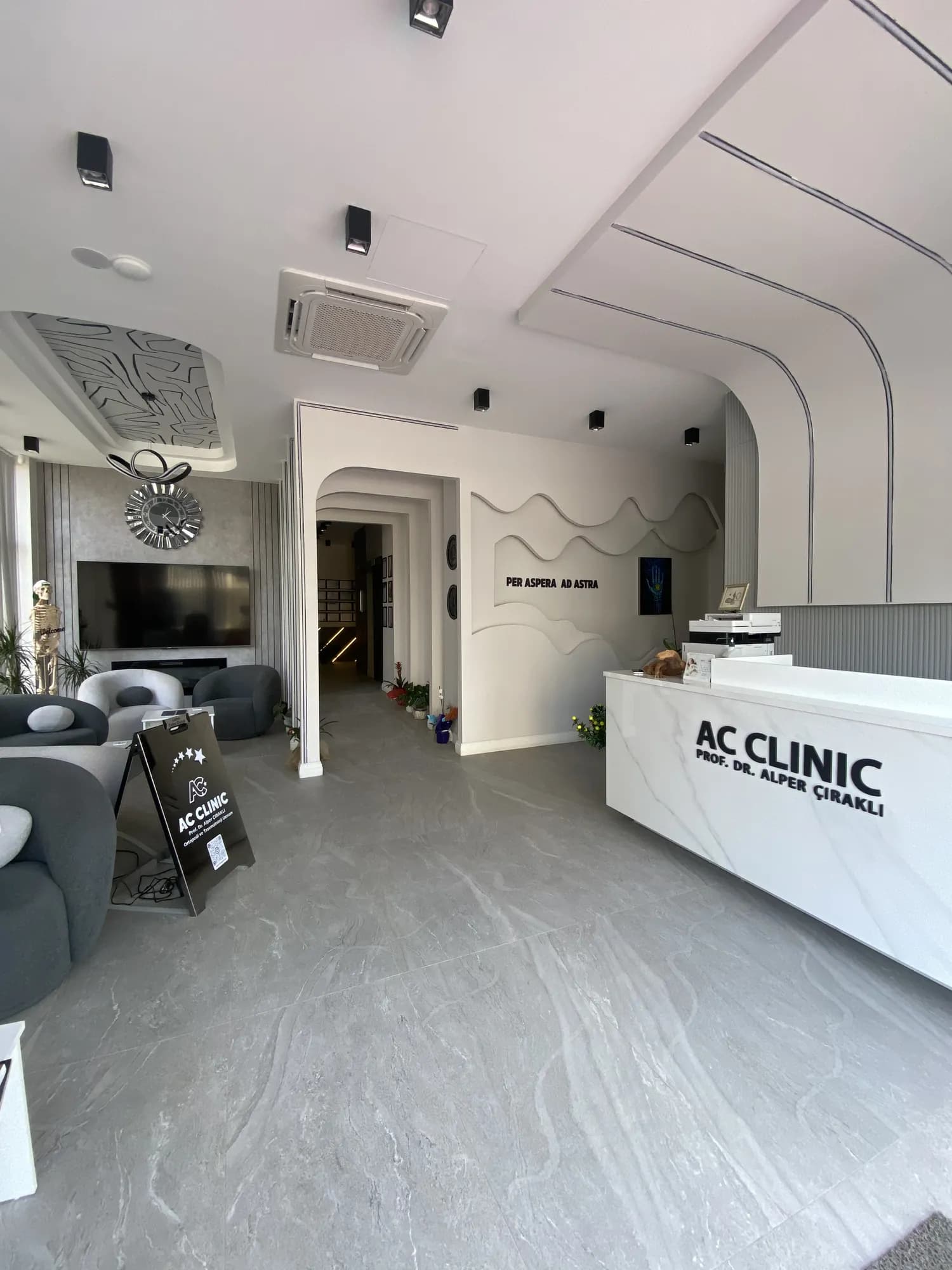AC CLINIC resepsiyonu — mermer banko ve 'Per Aspera Ad Astra' duvar yazısı